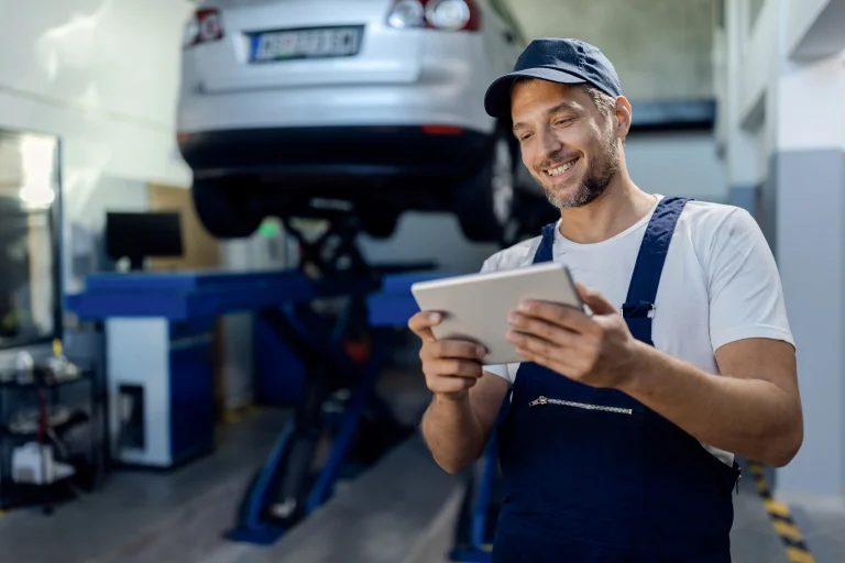 Garagiste travaillant en mobilité sur tablette autour du véhicule à réparer