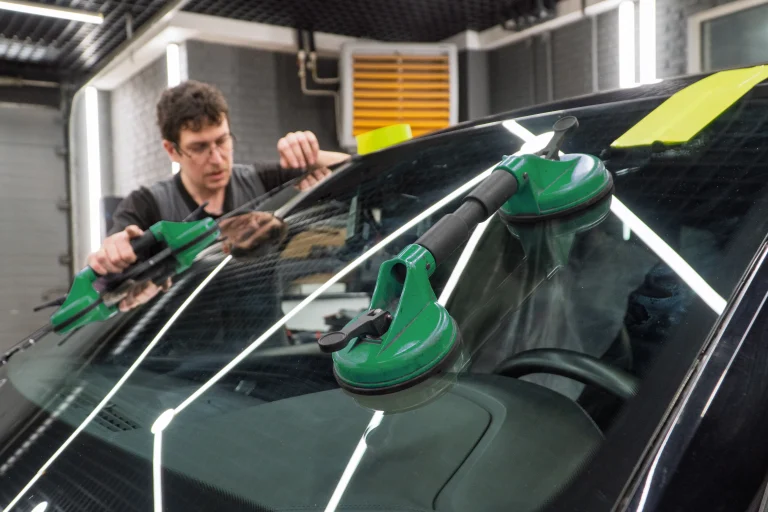 Technicien remplaçant un pare-brise à l’aide d’outils de levage spécialisés
